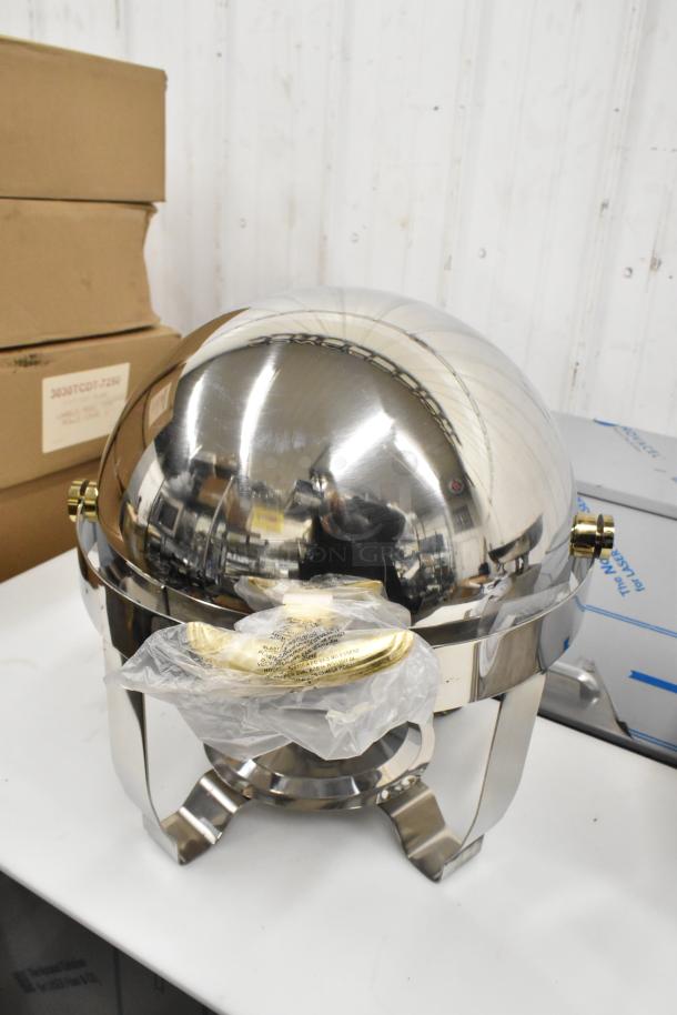 Stainless steel round roll top chafer, brand new with minor scratches, includes protective plastic cover and brass accents.