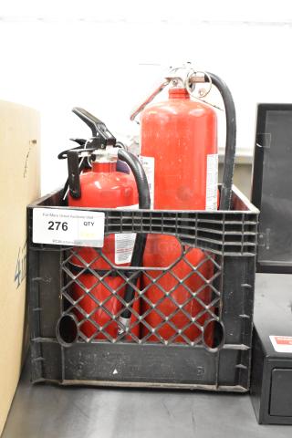 Five red fire extinguishers in a black crate. Labels visible; various sizes. Auction lot 276. Local pickup only.