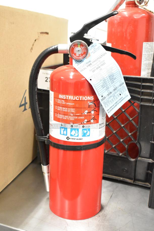 Five red fire extinguishers, First Alert brand, each with instructions and hose, sold as-is, pick-up only.