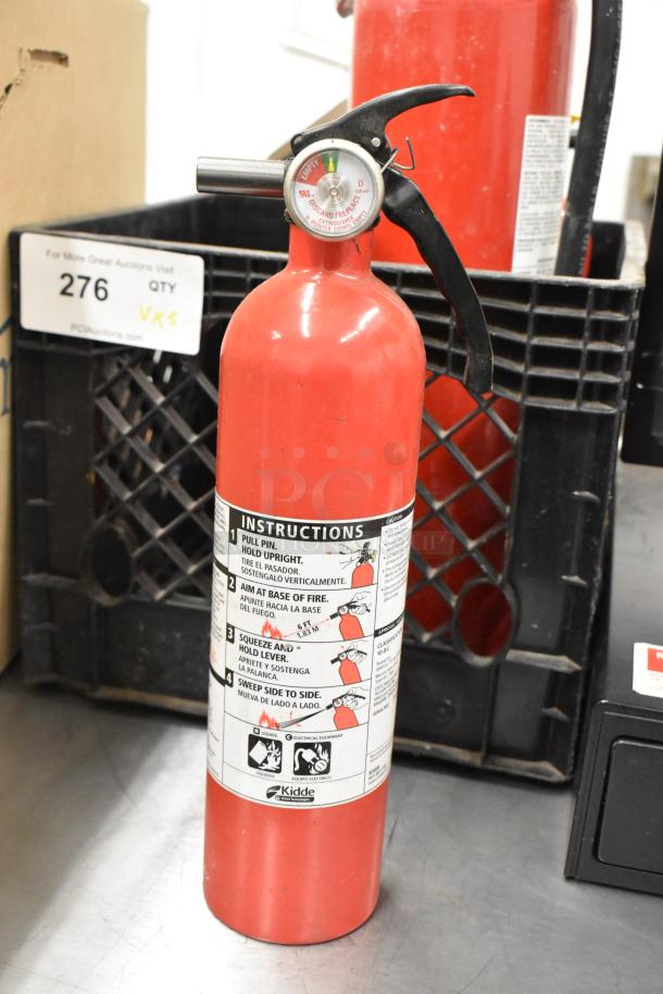 Red Kidde fire extinguisher with safety instructions visible; gauge reads "empty." In a crate with auction tag 276.