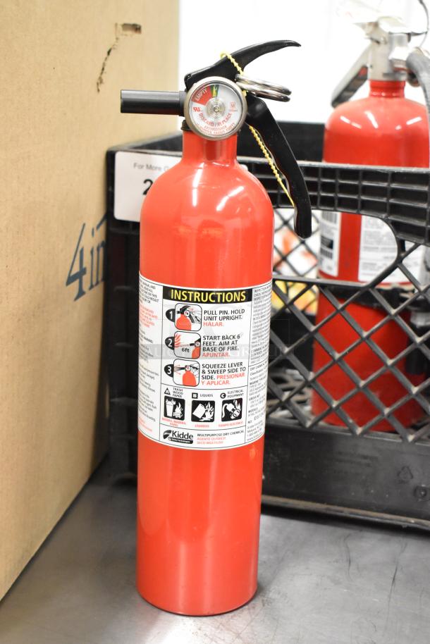 Red Kidde fire extinguisher with instructions label, gauge showing full, and black handle. Includes buyer pickup requirement.