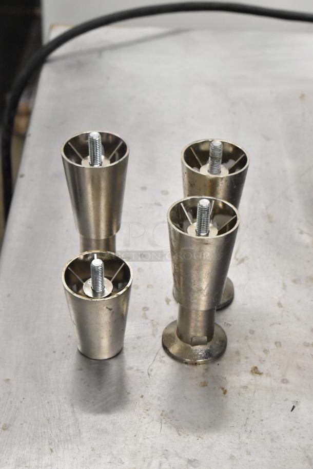 Four stainless steel feet with threaded bolts on a metal surface, likely replacement parts for a machine.