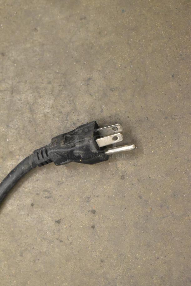 A close-up of a black three-prong electrical cord plug on a concrete surface.