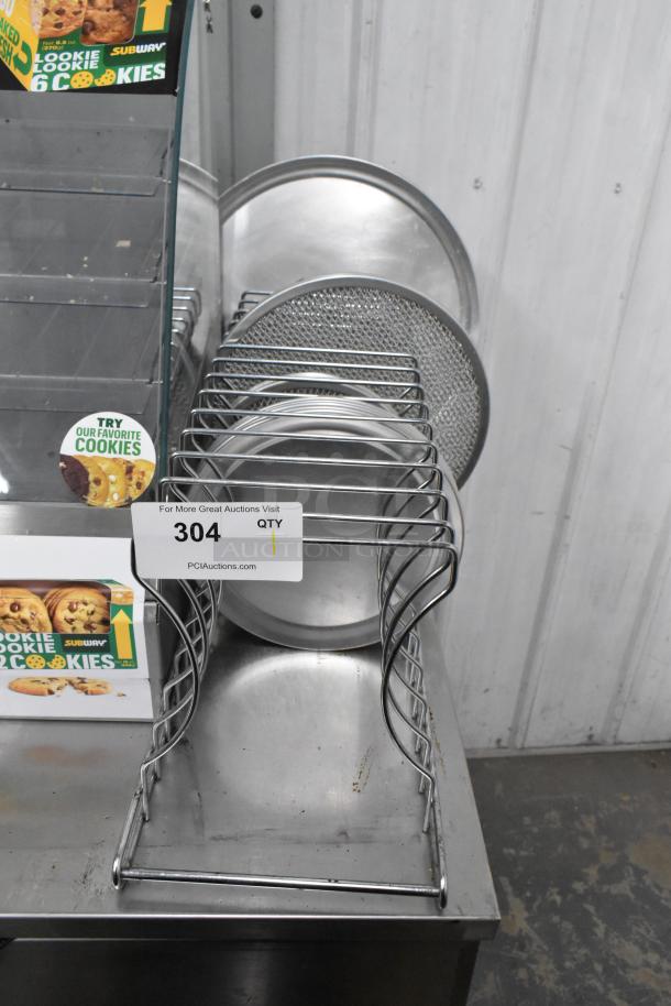 Metal countertop pizza pie pan rack with round metal pizza pans and screens, visible auction tag "304," in used condition.