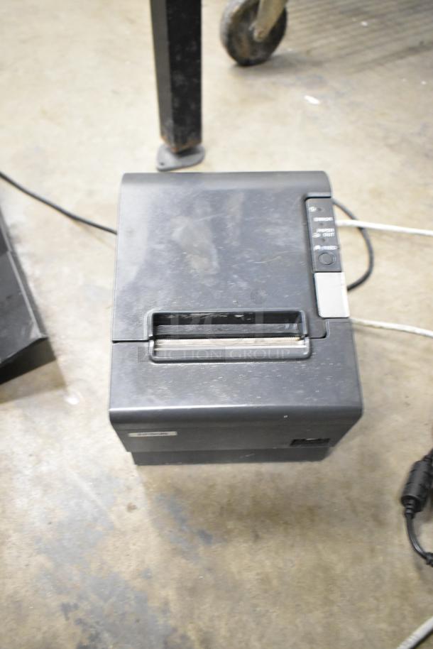 Epson receipt printer, black, with visible buttons and feed slot, in used condition on concrete floor.