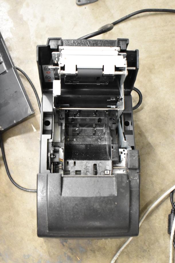 Epson receipt printer open for maintenance, showing internal mechanisms and wiring on a concrete floor.