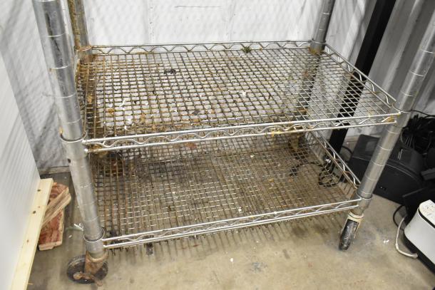 Chrome finish 3-tier wire cart on commercial casters, visible wear and rust, sturdy construction, ideal for storage or transport.