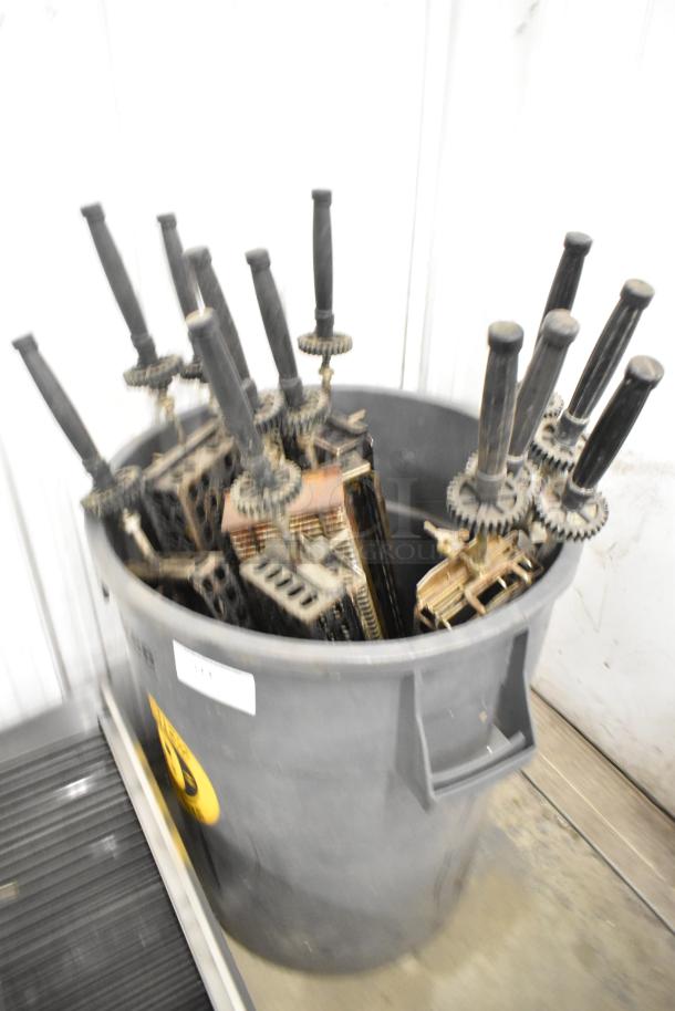 12 metal skewers for rotisserie oven, in gray poly trash can. Black handles, gears attached. Shows signs of use.