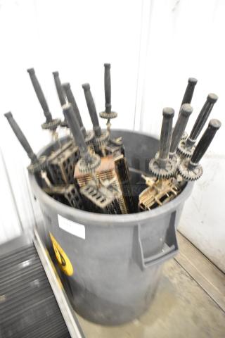 12 metal skewers for rotisserie oven, in gray poly trash can. Black handles, gears attached. Shows signs of use.