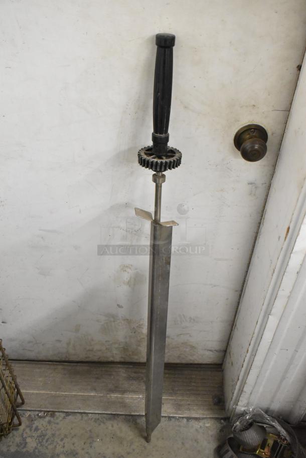 Metal skewer with black handle and gear mechanism for rotisserie oven. Shown against a white background.