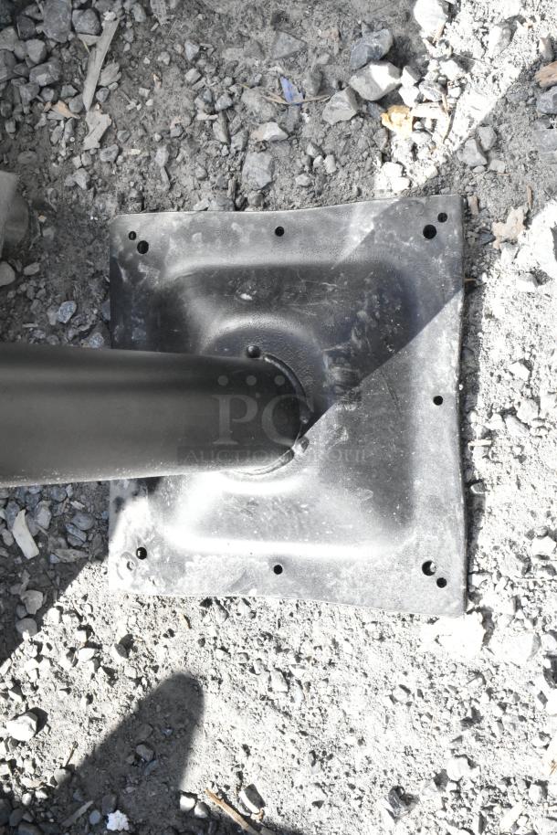 Brand new black metal table base column on gravel, scratch and dent visible, square plate with pre-drilled holes.