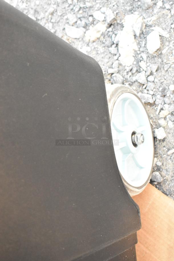 Brand new black poly ice bin with commercial casters on rocky ground. Scratch and dent model, durable construction.