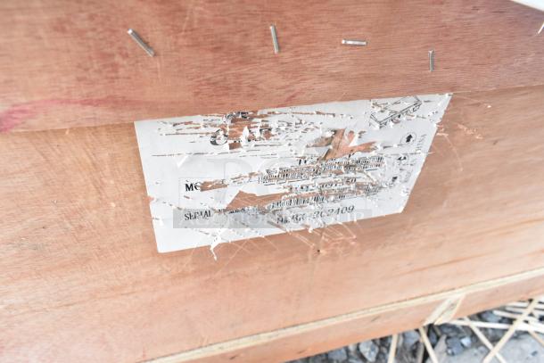 Wooden crate with scratched and torn shipping label, some text visible. Contains auction items: Regency dish table, Avantco griddle.