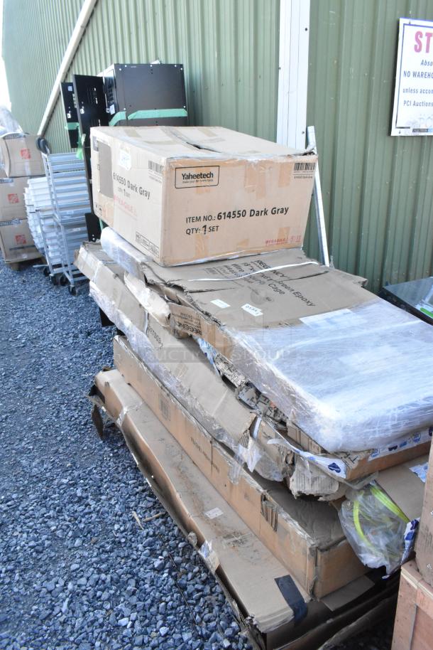 Cardboard boxes labeled "614550 Dark Gray" showing scratches and dents, on pallets. Includes Regency wire security cage and Steelton work table.