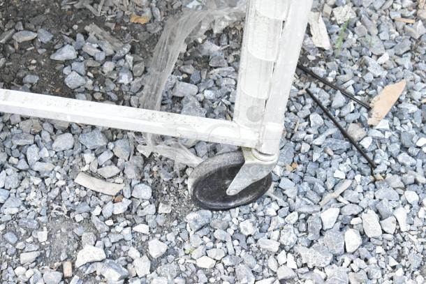 2 metal pan transport racks on commercial casters, shown on gravel surface, sturdy construction for industrial use.
