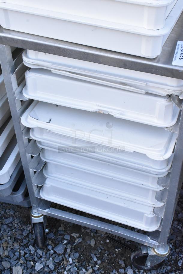 Metal pan transport rack with white poly dough bins on commercial casters, showing some wear at edges.