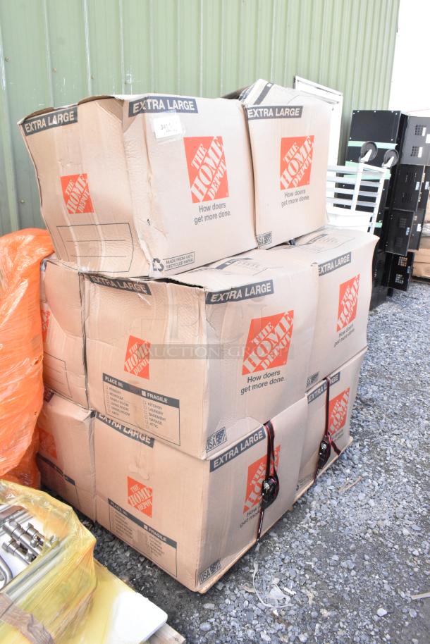 Six extra large Home Depot boxes containing various items like gray bus bins, a colander, and metal pieces, stacked on a pallet.