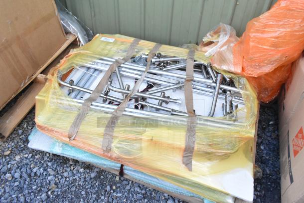 Lot of various stainless steel pieces wrapped in yellow and orange plastic. Items stored on wooden pallets.