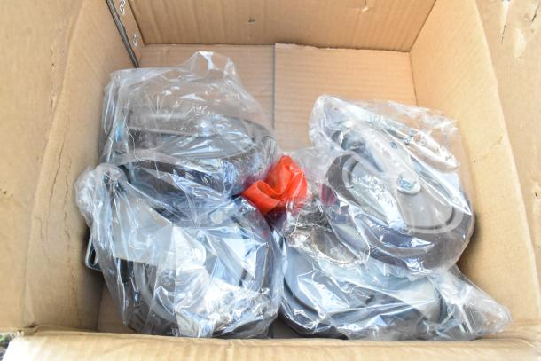 Box containing four commercial casters, each wrapped in plastic. New condition, heavy-duty design, suitable for industrial use.
