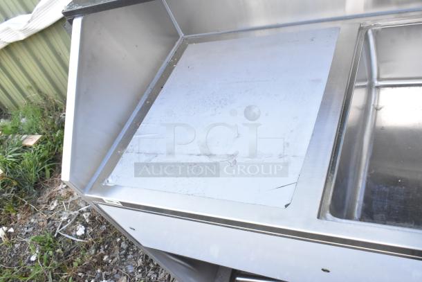 Brand new Regency 600PB63B 63" stainless steel portable bar with scratches, two speed rails, and ice bin, outdoor setting.