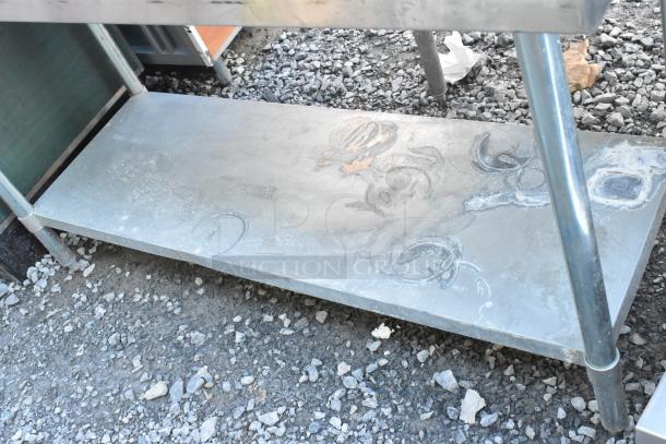 Stainless steel table with metal under shelf, showing surface wear and decorative markings. Solid construction.