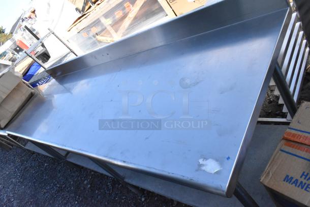 Stainless steel table with metal under shelf and back splash, showing signs of wear. Ideal for kitchens or workshops.