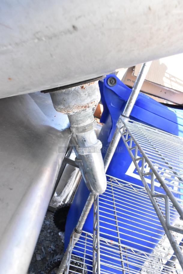 Stainless steel single bay wall mount sink with visible plumbing; appears in used condition, slight rust on pipe fittings.