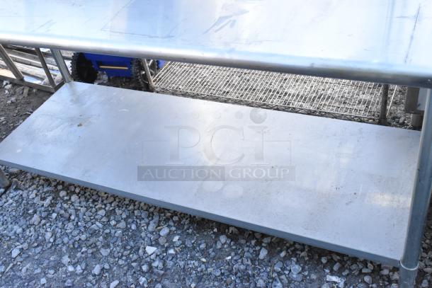 Stainless steel table with metal under shelf, visible wear; sturdy construction ideal for kitchen or industrial use.