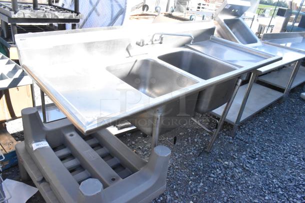 Stainless steel 2 bay sink with dual drain boards, faucet, and handles. Ideal for commercial use, in good condition.