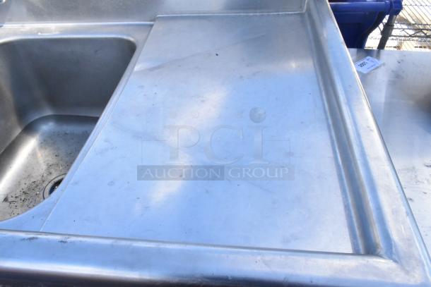 Stainless steel 2 bay sink with dual drain boards, faucet and handles. Some wear visible, suitable for commercial use.
