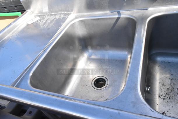 Stainless steel 2 bay sink with dual drain boards, faucet, and handles. Features some wear. Ideal for commercial use.