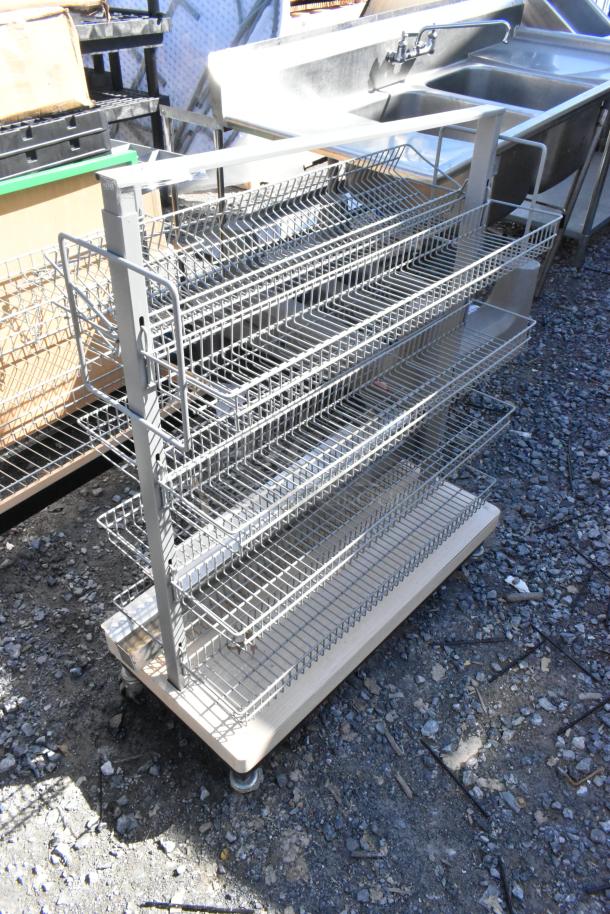 Metal display rack on casters with multiple wire shelves, showing minor wear. Ideal for retail display uses.