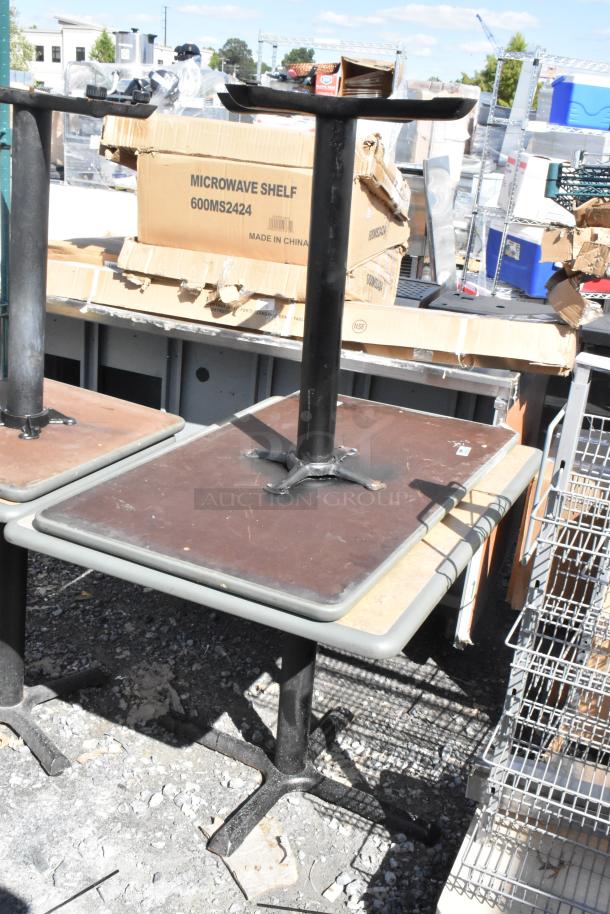 Four dining height tables with black metal bases and brown tabletops. Some wear visible. Auction lot.