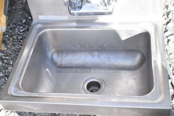 Stainless steel single bay wall mount sink with attached faucet and handles, minor surface wear visible.