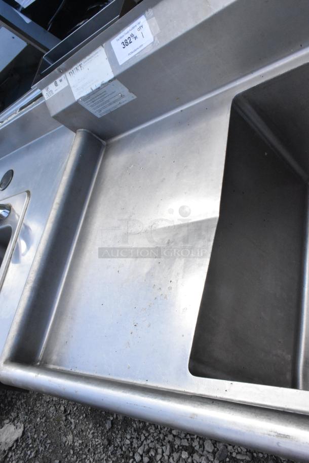 Stainless steel commercial 3 bay sink with dual drain boards, visible wear, labels showing brand "Duke" and item info.