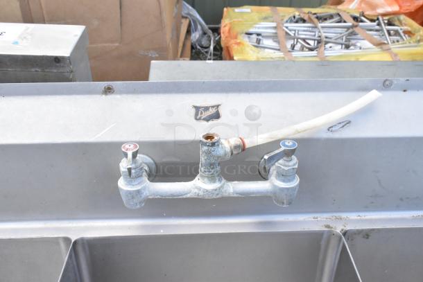 Stainless steel commercial 3 bay sink by Duke, with dual drain boards, showing used condition and visible faucet fixture.