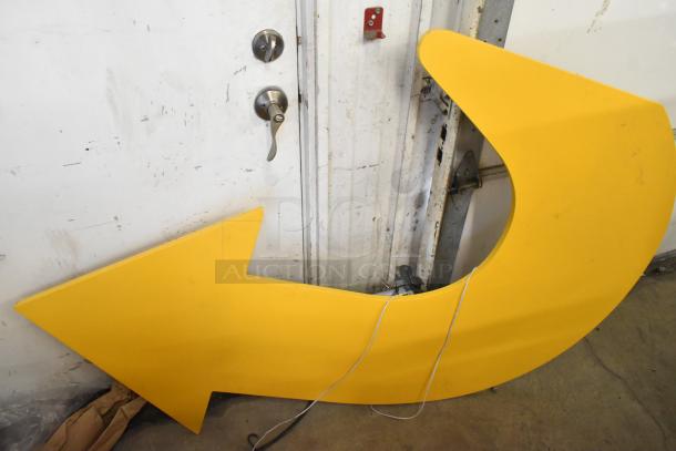 Yellow subway arrow sign in good condition, propped against a wall. No visible labels. Includes wiring details.