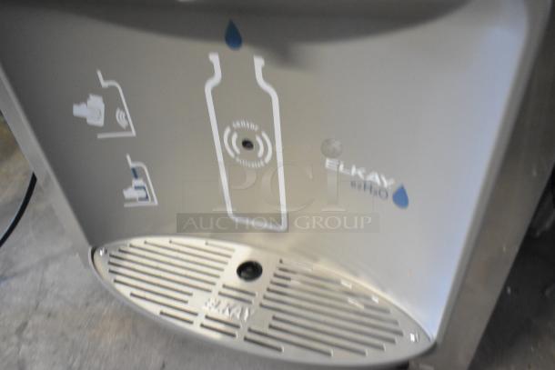 Brand new Elkay water fountain with bottle filler, showing minor scratches. Features sensor activation and Elkay logo.