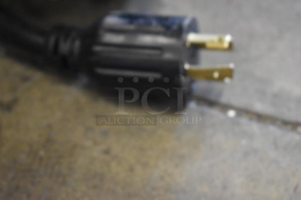 Blurred image of a black electrical plug on a countertop. No visible details of the Bunn IMIX-5 Cappuccino Machine.
