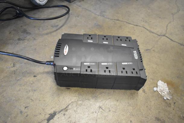 "CyberPower 485VA UPS with six outlets on a concrete floor, showing 'Surge' and 'Battery' labeled sockets."