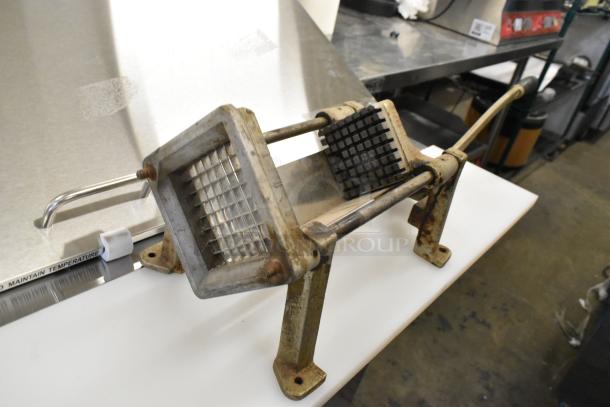 Metal countertop French fry cutter with lever and grid design, rusted condition, mounted on two legs for stability.