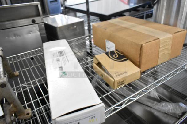 Lot of various items on metal shelf, including boxed Prince Castle 4 Channel Timer and Tripp Lite Unit. Items appear new.