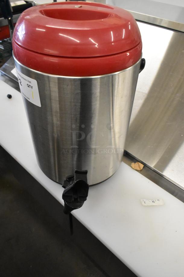 Stainless steel beverage holder dispenser with red lid and front spigot. Item label on side. Appears in good condition.