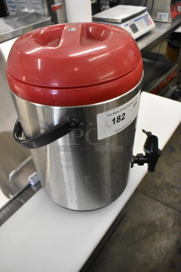 Stainless steel beverage dispenser with red lid, side handles, and a black spout. Label shows auction number 182.