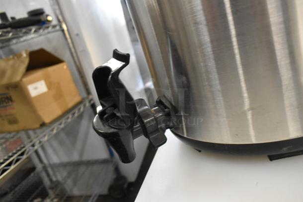 Metal beverage holder dispenser with black spigot, stainless steel body, and minor scuffs. Suitable for liquids.