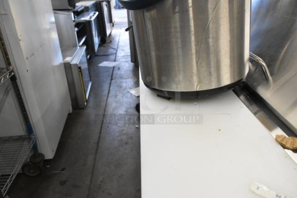 Stainless steel metal beverage holder dispenser, cylindrical shape, positioned on a countertop, showing some surface wear.