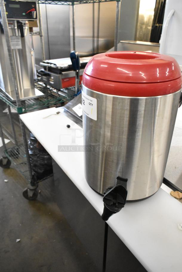 Stainless steel beverage dispenser with red lid and black spigot. Includes visible sticker indicating item 132. Good condition.