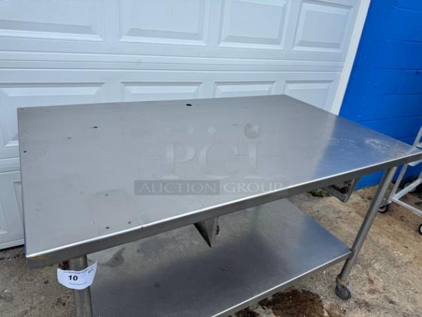 60" stainless steel work table with undershelf, on casters. Slight surface wear. Auction tag "10" attached.