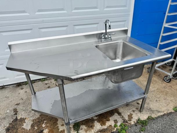 Stainless steel 60" sink with table, features broken faucet. Includes side workspace and lower shelf. Good for kitchen use.