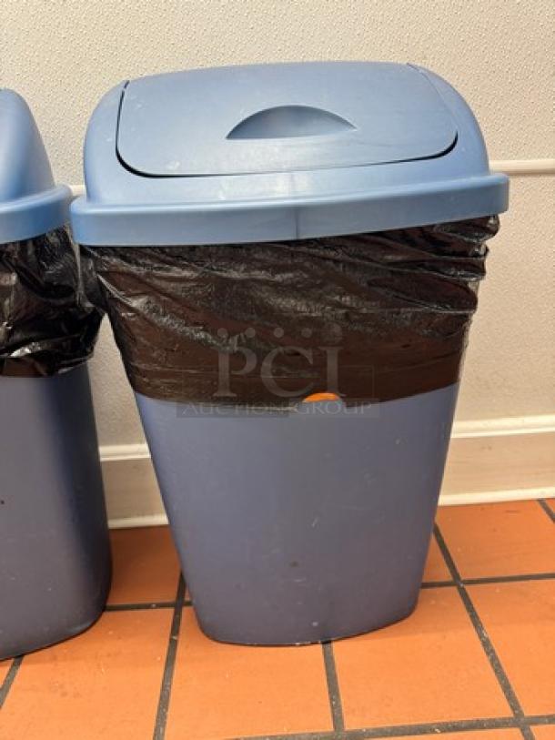 Blue Swing Top Waste Can BIDX2, used condition, with black trash bag. Sturdy design, ideal for office or home use.